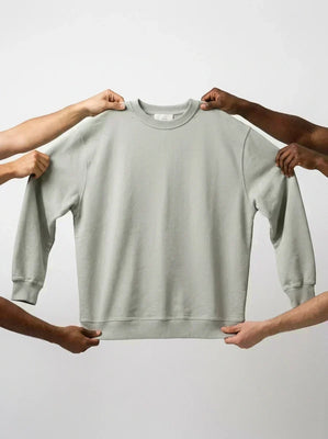 Sage green sweatshirt held up by four hands showing product fit and colour.