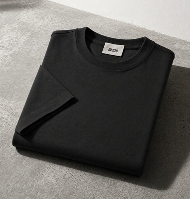 Black crewneck sweatshirt folded on a gray concrete surface with a white wall in the background.