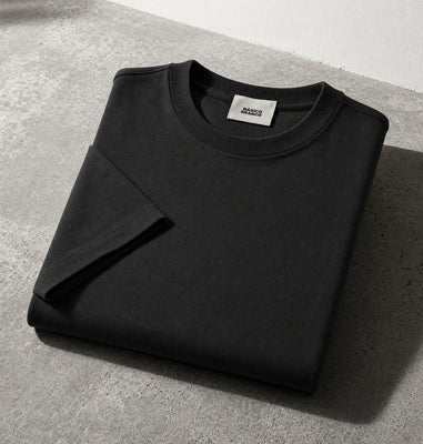 Black crewneck sweatshirt from Basico Branco, folded on a gray concrete surface with a white wall background.