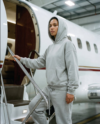 Woman in grey hoodie and joggers by Basico Branco stepping into private jet interior.