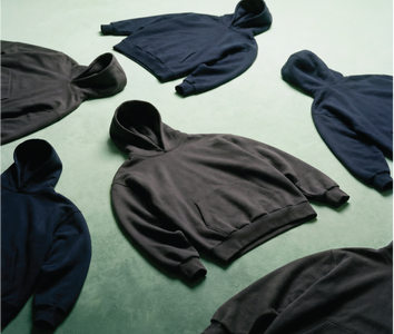 Multiple hoodies by Basico Branco laid out on green surface in minimal product arrangement.