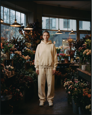Model wearing a beige Basico Branco hoodie and matching sweatpants while standing inside a flower shop.