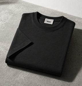 Black crewneck sweatshirt folded on a gray concrete surface with a white wall in the background.