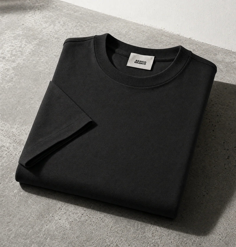 Black crewneck sweatshirt from Basico Branco, folded on a gray concrete surface with a white wall background.
