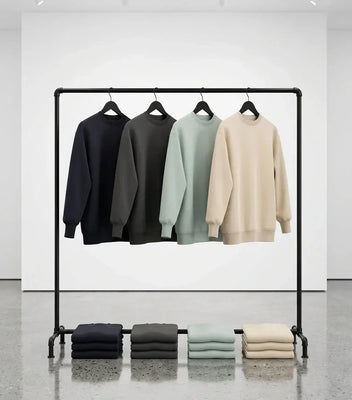 Four sweatshirts displayed on a black pipe rack with folded sweatshirts underneath in navy, charcoal, sage, and cream.