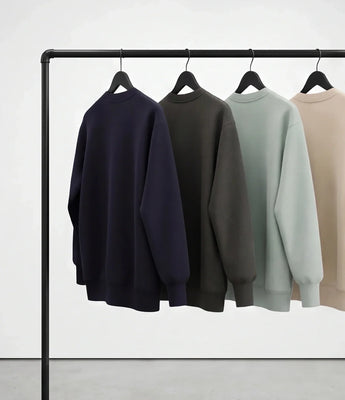 Four sweatshirts in navy, charcoal, sage, and beige from Basico Branco hanging on a black rail against a white background.