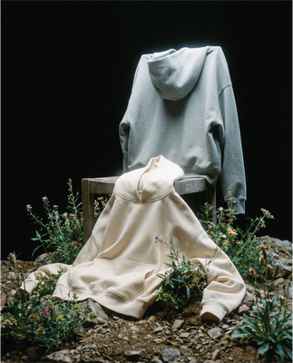 Basico Branco grey and cream hoodies draped over a wooden chair in a natural wildflower setting.
