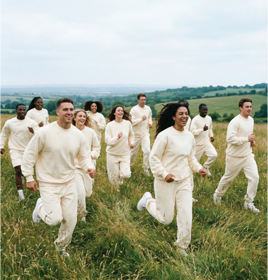 Group in cream sweats by Basico Branco running through open field in natural outdoor setting. 