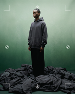 Basico Branco charcoal hoodie worn against a green backdrop with stacked apparel below.