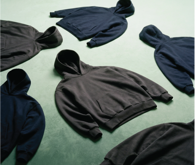 Multiple hoodies by Basico Branco laid out on green surface in minimal product arrangement. 