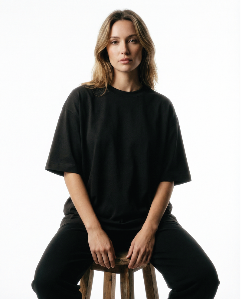 Woman wearing a black Basico Branco oversized organic cotton T-shirt while seated on a stool in a minimalist studio.