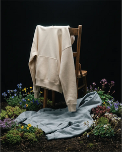 Cream hoodie and joggers by Basico Branco styled on chair with flowers against dark backdrop.