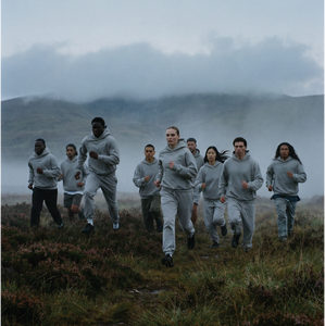 Group of runners in grey hoodies and joggers by Basico Branco moving through misty outdoor landscape. 