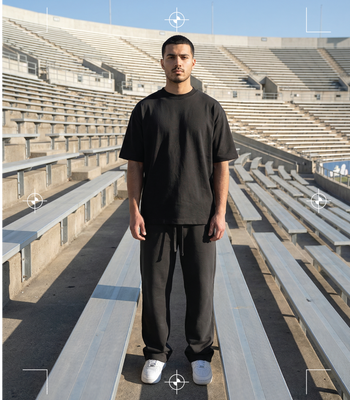 Minimalist black tee and joggers by Basico Branco worn in empty stadium bleachers. 